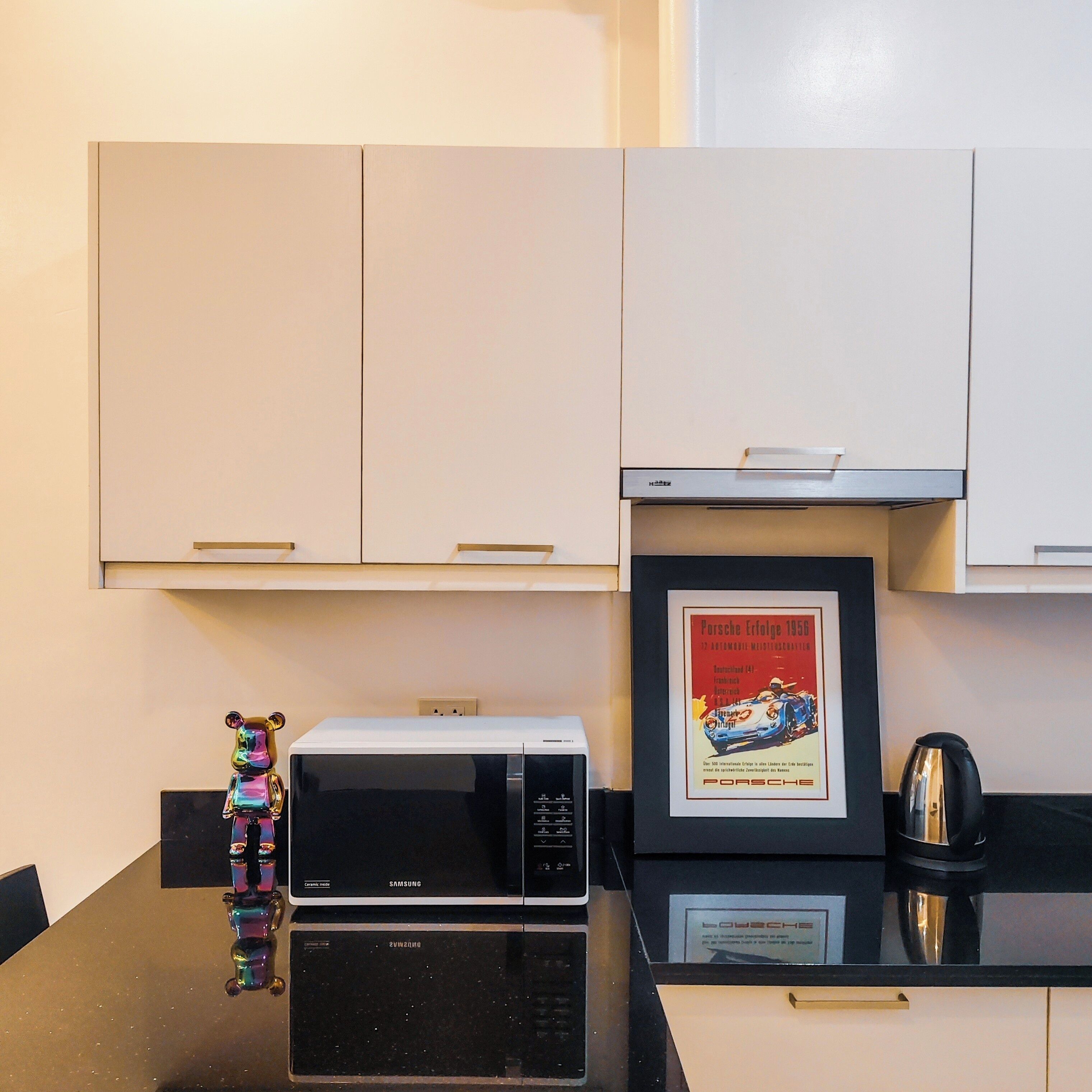 Uma cozinha com armários brancos, micro-ondas, um pôster emoldurado e um objeto decorativo sobre a mesa.