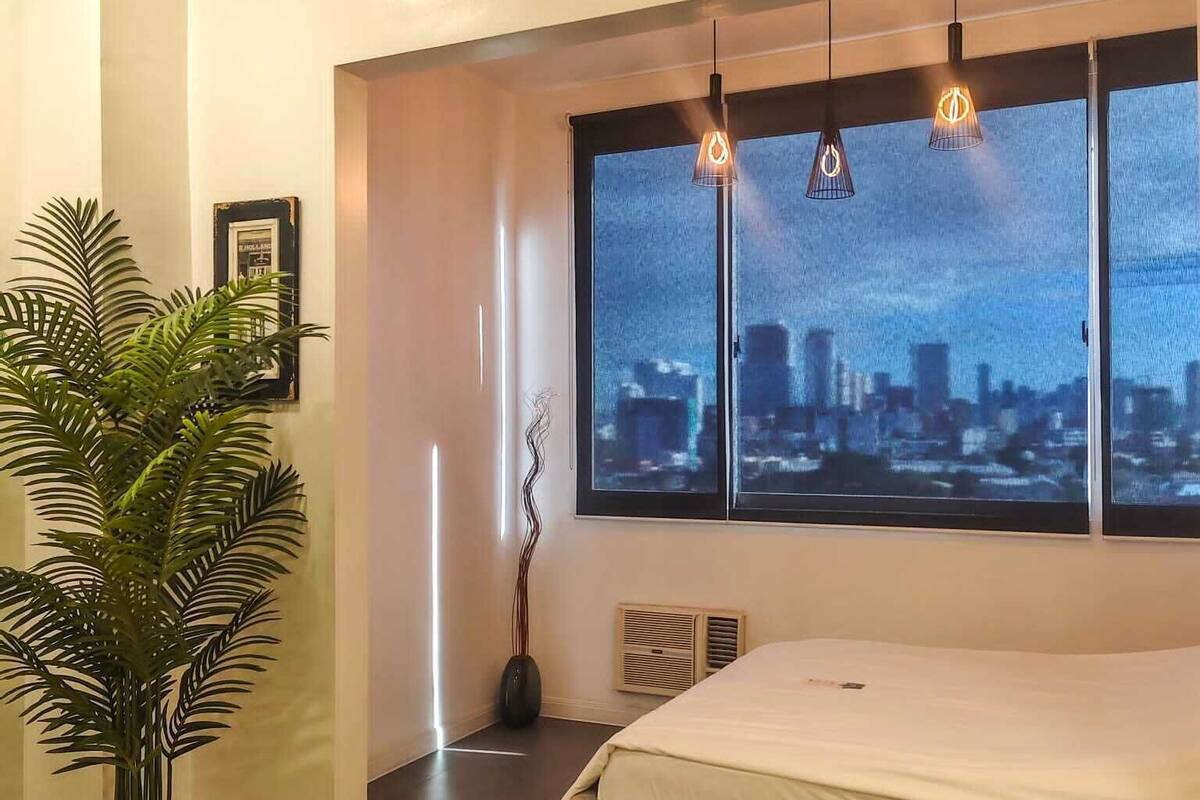 A bedroom with a large window, a potted plant, and a radiator.