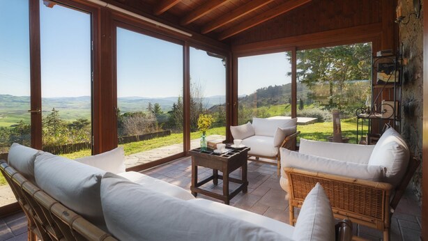 A sunlit room with large windows, a wooden ceiling, and a view of rolling hills. - Podere Il Chiesino 8 2 (Montecatini Val di Cecina)