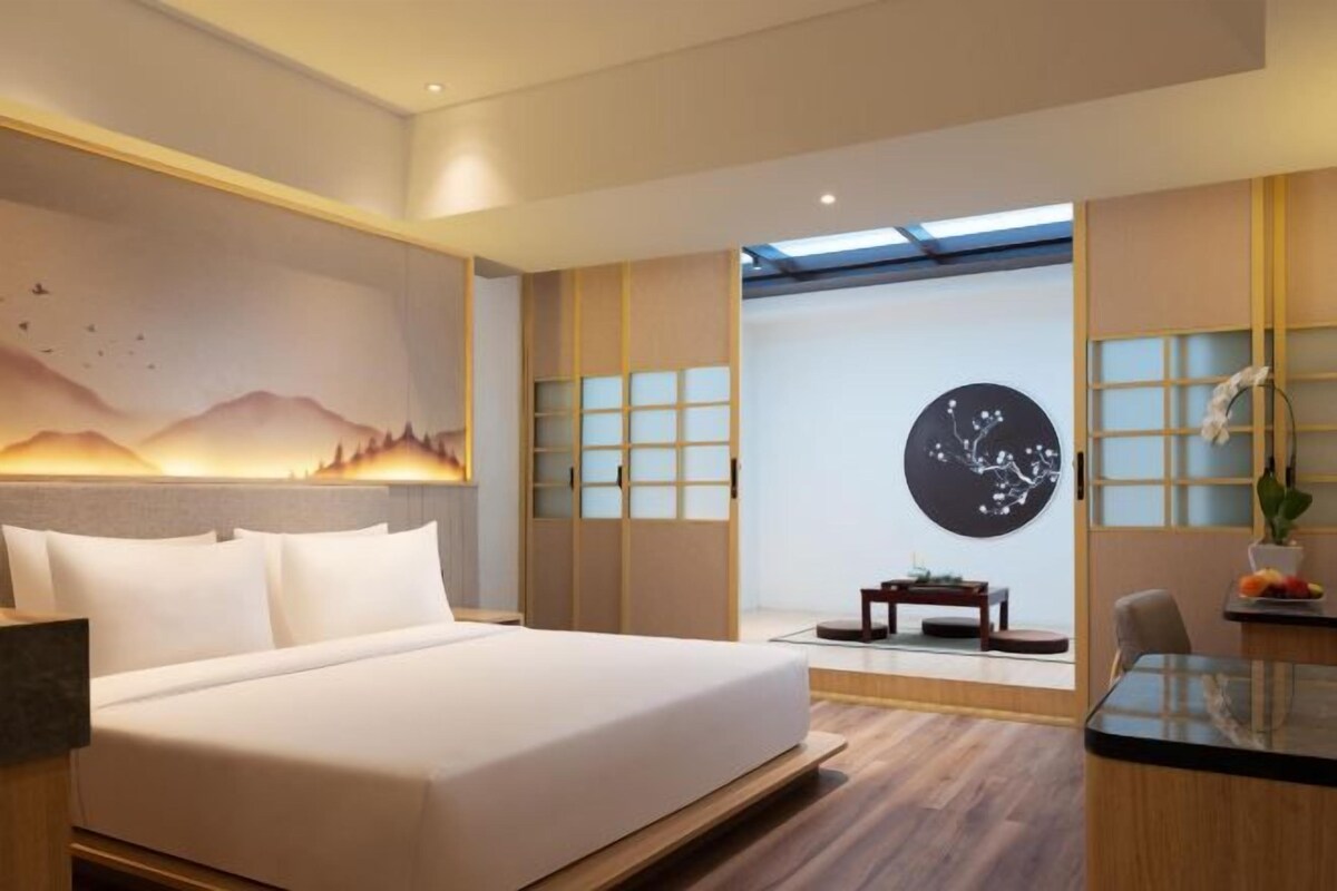 Una habitación de hotel moderna con una cama grande, un escritorio y vistas de la ciudad a través de un ventanal amplio.
