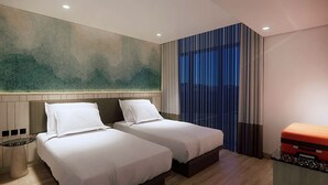 Habitación de hotel con dos camas, un mural abstracto grande en la pared, una mesita de noche y una maleta sobre una mesa.