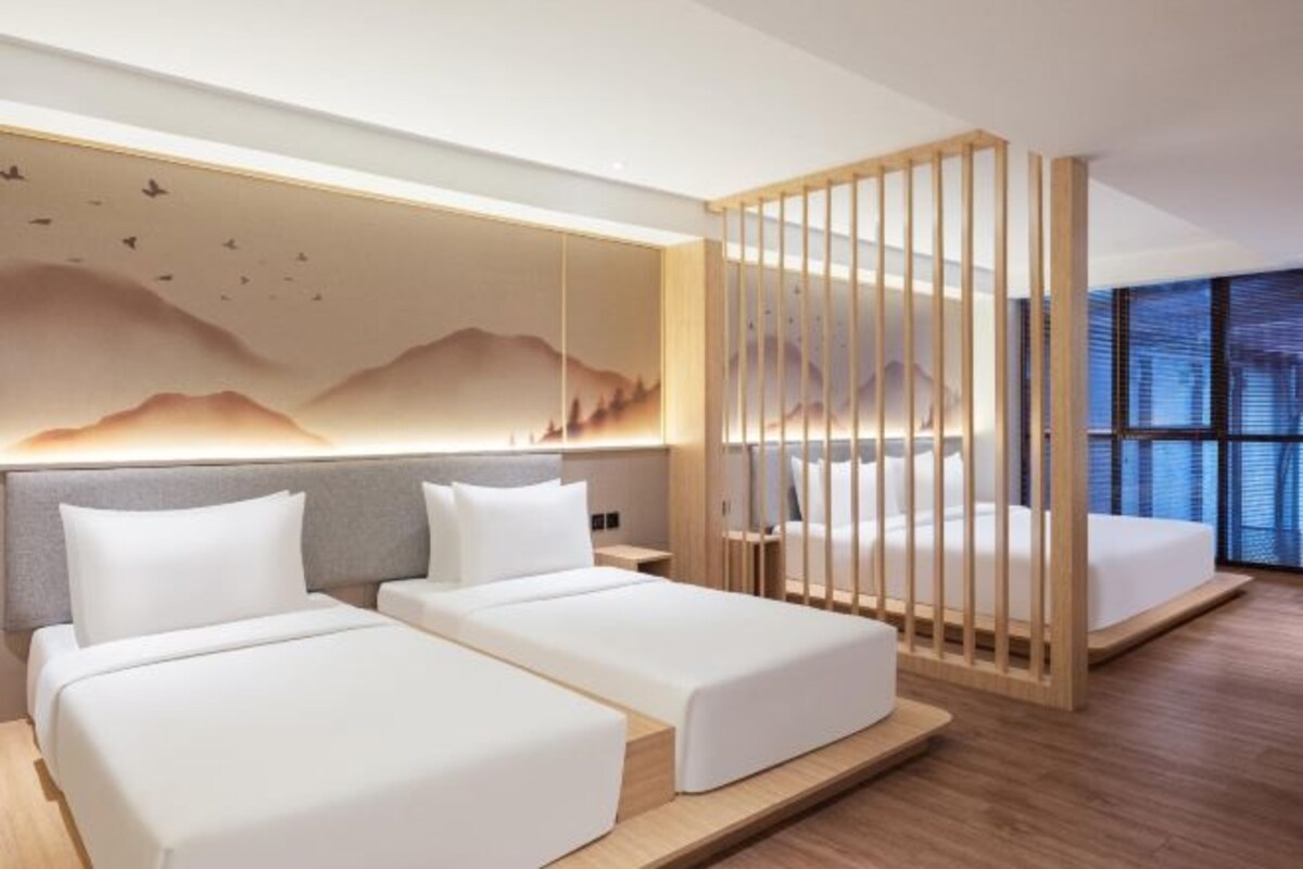 Una habitación de hotel moderna con dos camas individuales, un separador de madera y un ventanal con vistas a la ciudad.