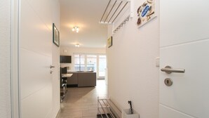 Corredor que dá para uma sala de estar com sofá, televisão e janela com vista para o exterior.