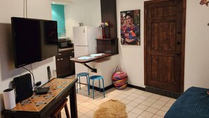 A compact living space with a kitchenette, a TV, a dining area with stools, and a large wooden door. - CDP 106 · Cute 1 bedroom in the Malecon (Puerto Peñasco)