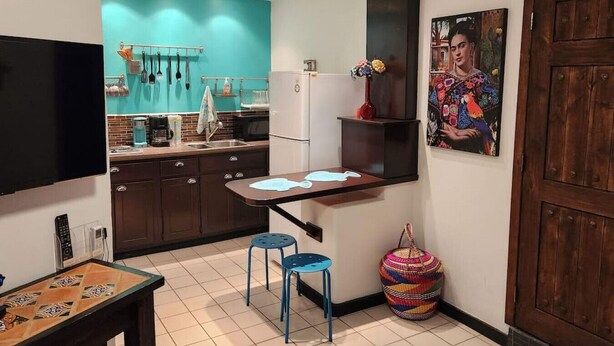 A compact kitchen with a teal backsplash, a refrigerator, and a small dining area with stools. - CDP 106 · Cute 1 bedroom in the Malecon (Puerto Peñasco)
