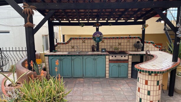 An outdoor kitchen area with a tiled backsplash, green cabinets, and a curved bar counter.