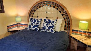 A bed with a blue quilt, two patterned pillows, a tiled headboard, and two bedside lamps.