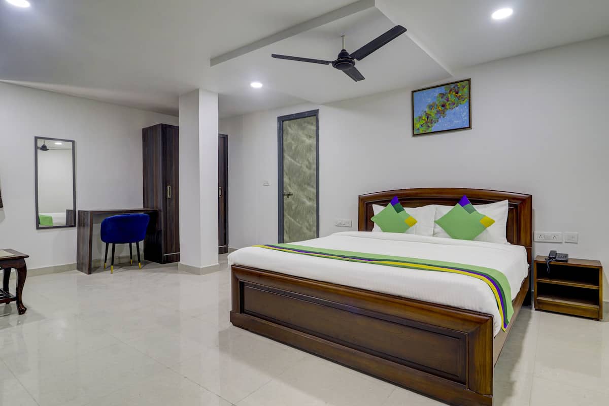A hotel room with a wooden bed, a desk, a chair, a ceiling fan, and a painting on the wall.