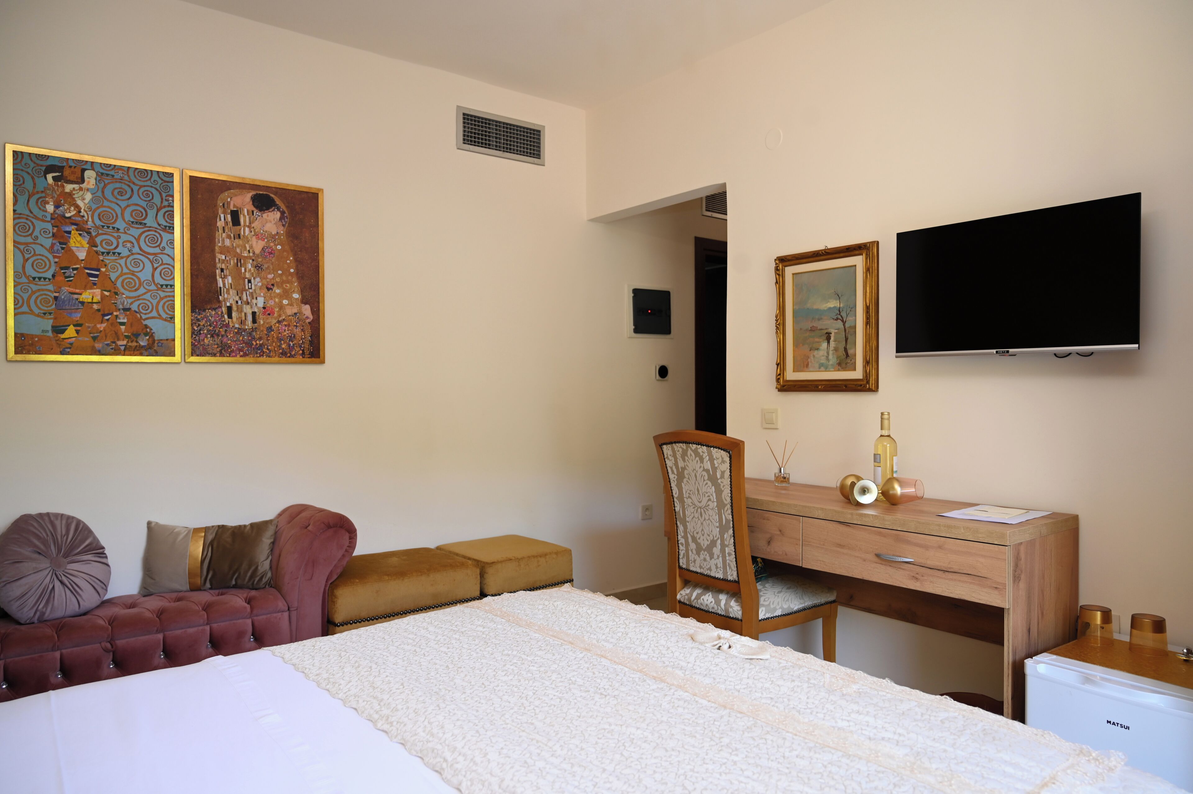 Habitación de hotel con cama, escritorio de madera, silla, televisión y dos cuadros en la pared.