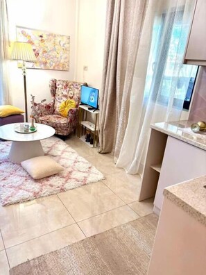 A living room with a round table, a floral armchair, a computer, and a window with curtains. - Ducato di Aria  (Nafplio)