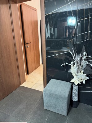 A room with a wooden door, a black tiled wall, a grey bench, and a vase with white flowers. - Ducato di Aria  (Nafplio)