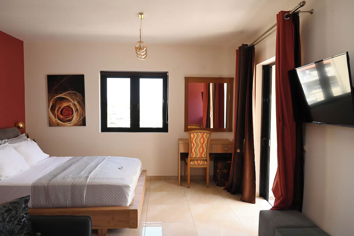 A bedroom with a bed, a desk, a chair, a TV, and a window.