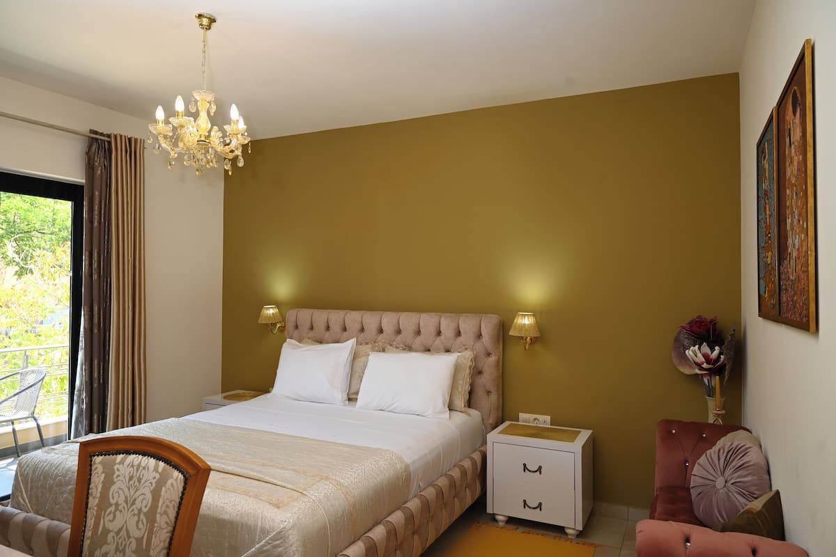 A bedroom with a large bed, a chandelier, a nightstand, a chair, and a painting on the wall.
