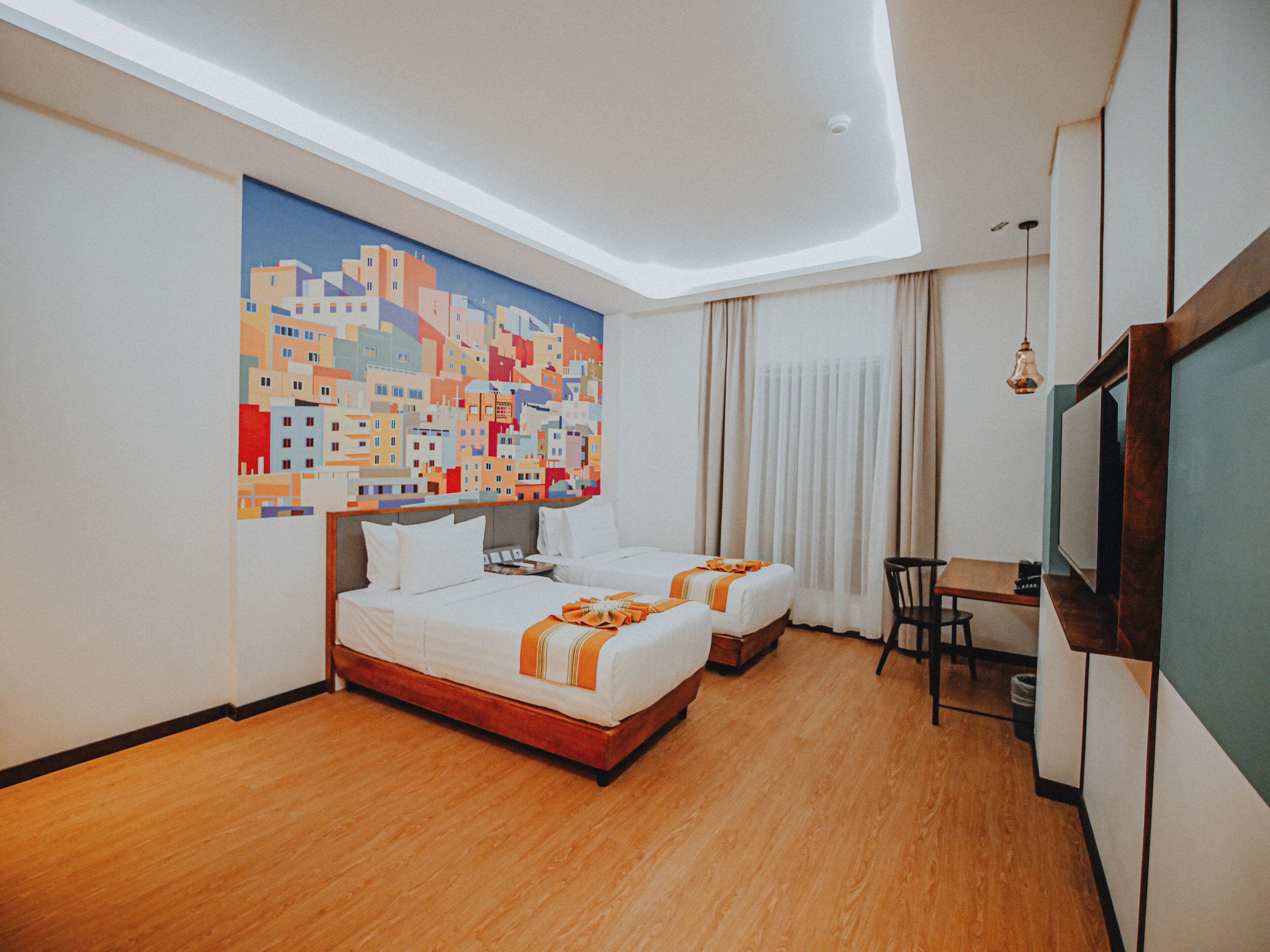 A hotel room with two beds, a painting of a cityscape, a desk, and a television.