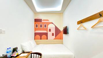 Una habitación pequeña y ordenada, con cama, escritorio y televisor en la pared.