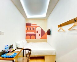 Una habitación pequeña y ordenada, con cama, escritorio y televisor en la pared.