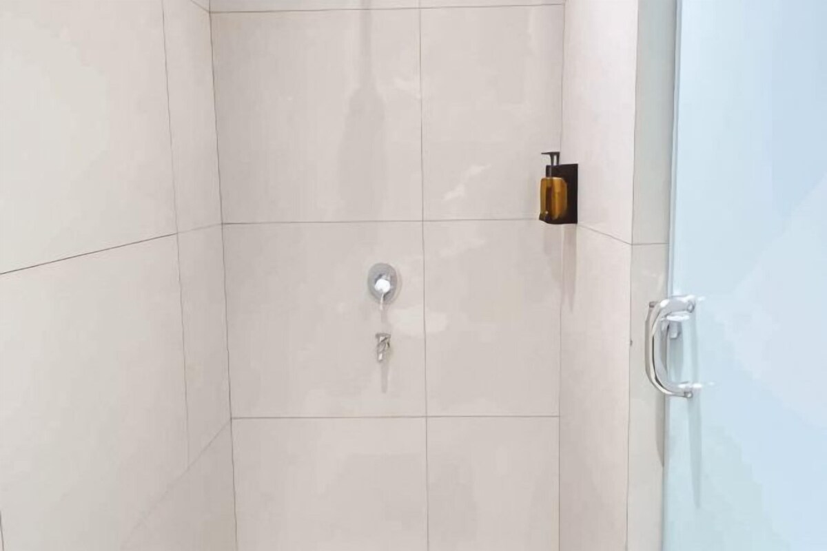 Un espace douche doté d’une porte en verre, d’un pommeau de douche et d’un distributeur de savon.