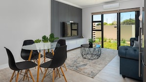 Un salon moderne avec une table à manger en verre, des chaises noires, un canapé bleu et un téléviseur fixé au mur.