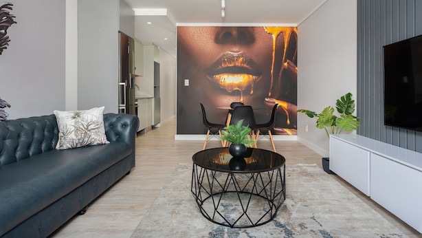Un salon moderne avec un canapé en cuir noir, une table basse ronde et une grande fresque murale.