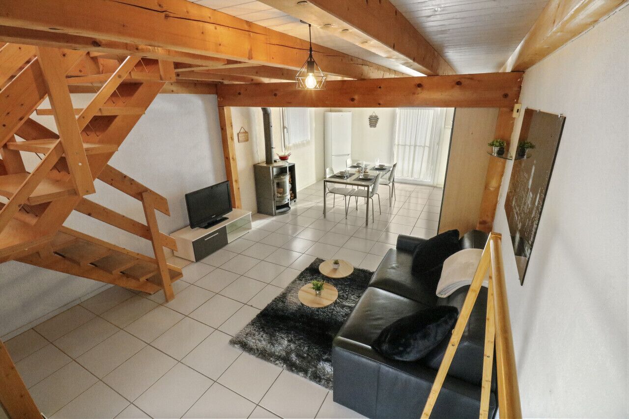 Uma sala de estar ampla com escada de madeira, um sofá, uma mesa de jantar e uma lareira.
