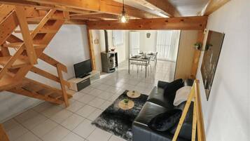 Uma sala de estar ampla com escada de madeira, um sofá, uma mesa de jantar e uma lareira.