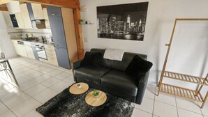 A modern living room with a black leather sofa, two round wooden side tables with plants, a black shag rug, a cityscape painting, and a wooden rack. - Charming duplex with a shared pool (Cournillens)