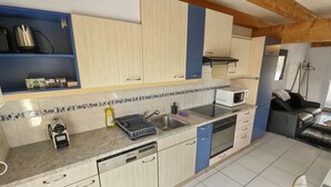 A kitchen with light wooden cabinets, a microwave, a dishwasher, and a sink. - Charming duplex with a shared pool (Cournillens)