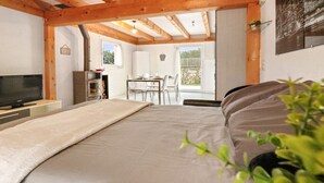 A bedroom with a bed, a TV, a wooden ceiling, a dining area with chairs, and a view of the outdoors. - Charming duplex with a shared pool (Cournillens)