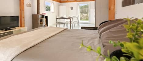 A bedroom with a bed, a TV, a wooden ceiling, a dining area with chairs, and a view of the outdoors.