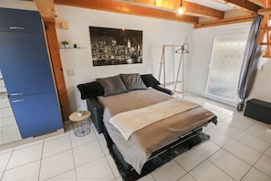 A bedroom with a bed, a wardrobe, a cityscape painting, a ladder, and a window with curtains.
