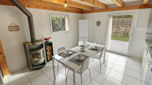 A modern kitchen with a dining area, a wood-burning stove, and a view of the garden. - Charming duplex with a shared pool (Cournillens)