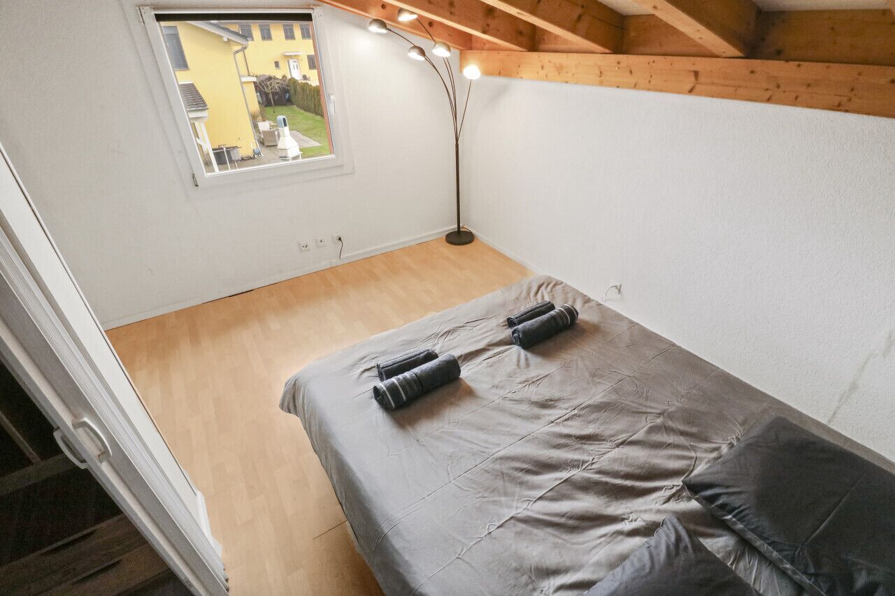 A small, compact room with a bed, a window, and a floor lamp.