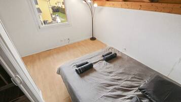 A small, compact room with a bed, a window, and a floor lamp.