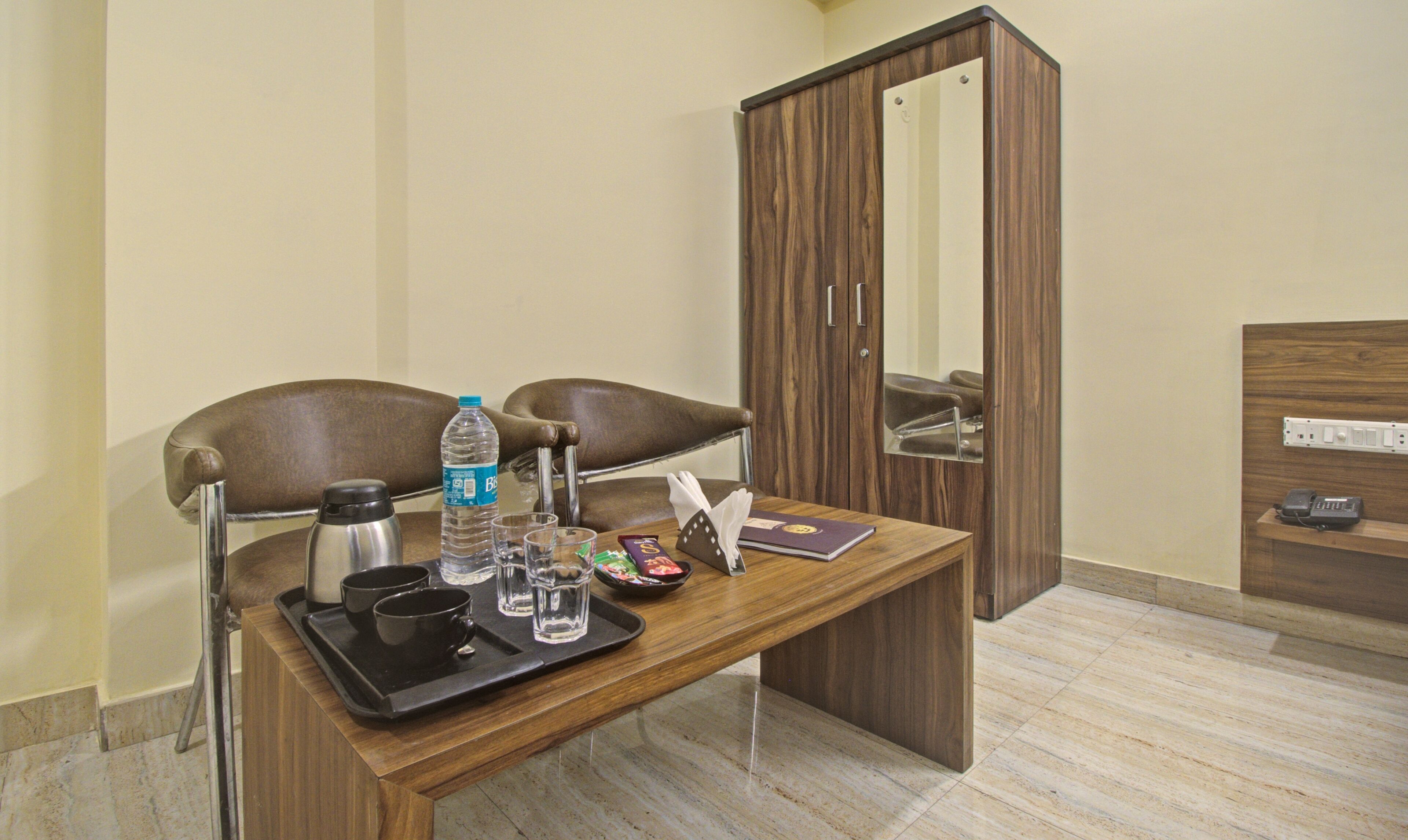 A hotel room with a wooden desk, two chairs, a minibar, a mirror, and a telephone.