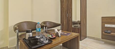 A hotel room with a wooden desk, two chairs, a minibar, a mirror, and a telephone.