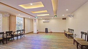 A conference room with a wooden floor, ceiling lights, a fan, and a potted plant.