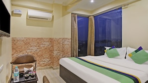 A hotel room with a bed, a small table with a tray, a chair, and an air conditioning unit on the wall.