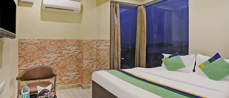 A hotel room with a bed, a small table with a tray, a chair, and an air conditioning unit on the wall.