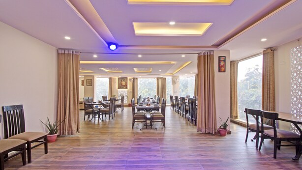 A spacious dining hall with a long table and chairs, large windows, and a ceiling with recessed lighting.