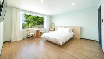 A modern hotel room with a large bed, a small desk, a chair, and a window with a view of trees.