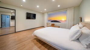 Ein Hotelzimmer mit Bett, Fernseher, Fenster mit Sonnenuntergangblick, einem kleinen Tisch und einem Stuhl.
