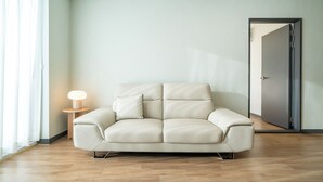 En moderne stue med en lysegrå sofa, et lille sofabord med en lampe og en dør i baggrunden.