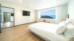 A hotel room with a bed, a TV, a window with a view, and a small table with a chair.