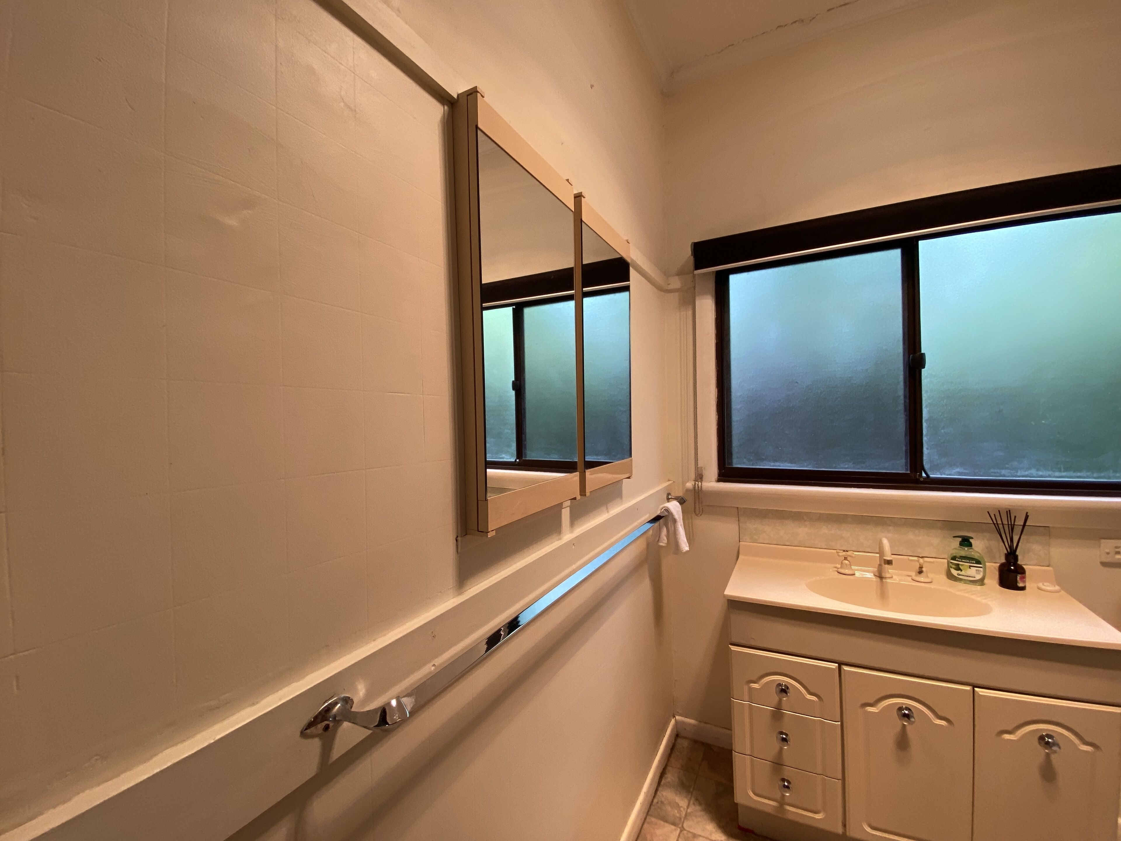 Une salle de bain avec une fenêtre, un miroir, un lavabo et un porte-serviettes.