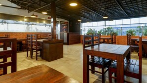 A restaurant interior with brick walls, wooden tables and chairs, and large windows. - Treebo Blueberry Inn (Bengaluru)