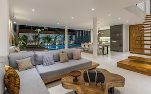 Een moderne woonkamer met een grijze modulaire bank, een houten salontafel en een trap.