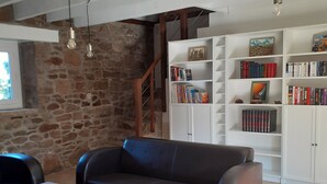Una sala de estar con una pared de piedra, una escalera, una estantería y un sofá de cuero.