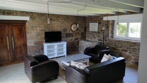 Una sala de estar con paredes de piedra, un mueble de madera, un televisor sobre un soporte blanco y sofás de cuero.
