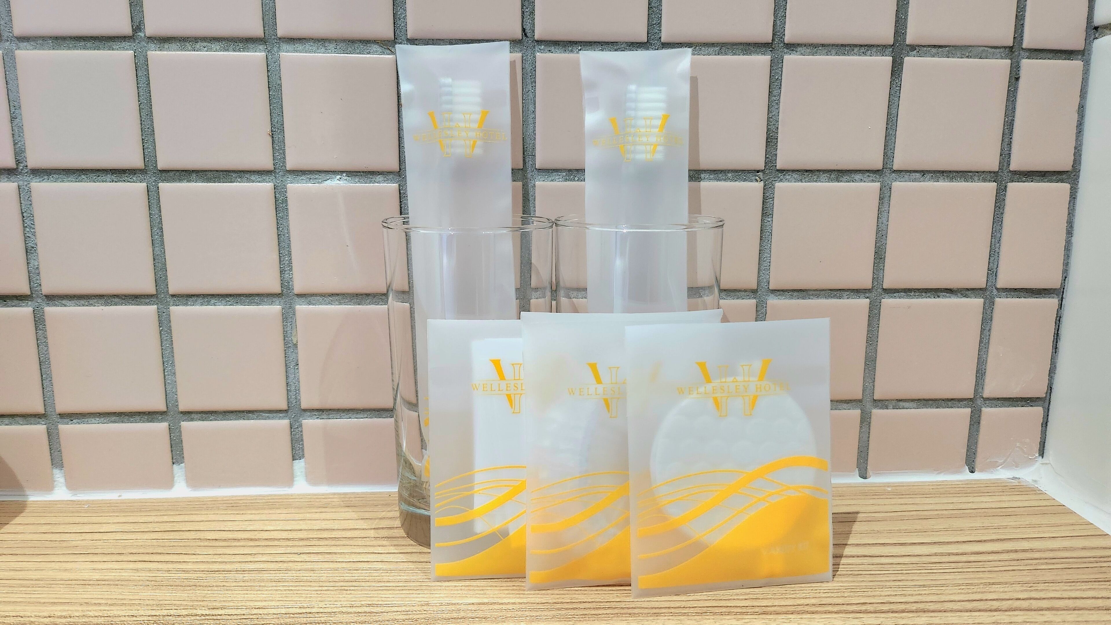 Un conjunto de cristalería transparente y bolsas de papel blancas con texto en amarillo sobre un muro de azulejos.