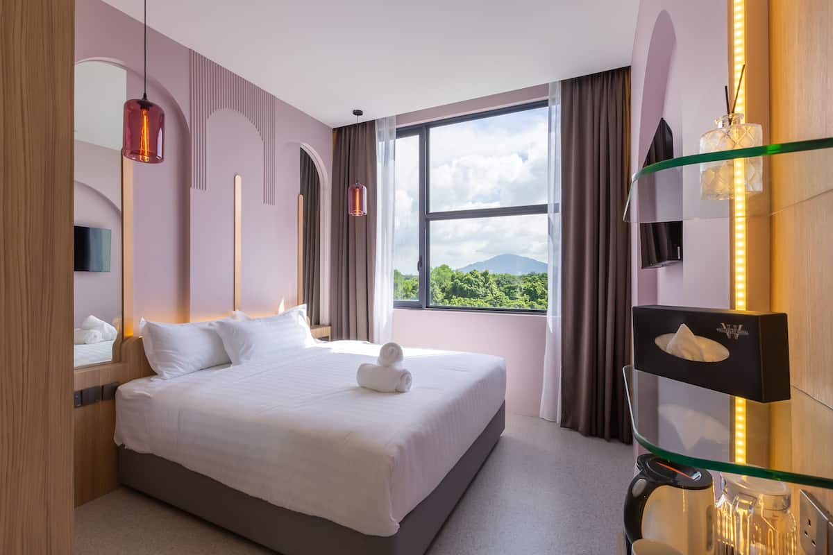 A hotel room with a large bed, a glass shelf with toiletries, a window with a mountain view, and a modern design.